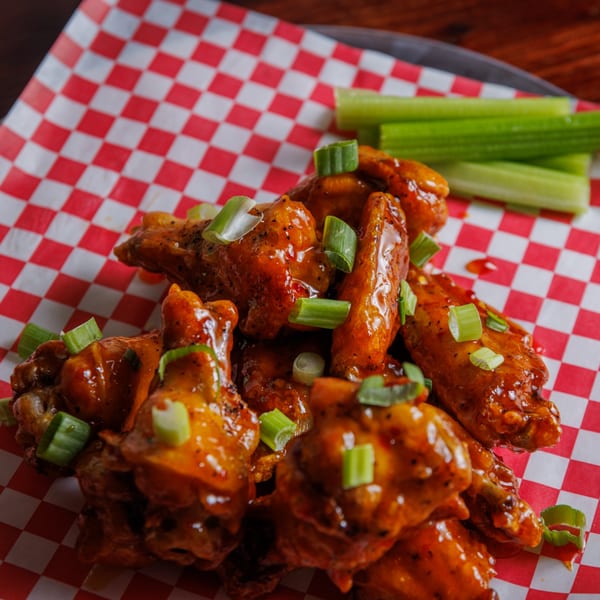 A plate of The Heights Pizzeria and Drafthouse's chicken wings with celery sticks on red and white checkered paper.