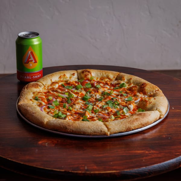 A Heights Pizzeria pizza with chicken, red onions, green onions, and sauce, next to a green beer can.