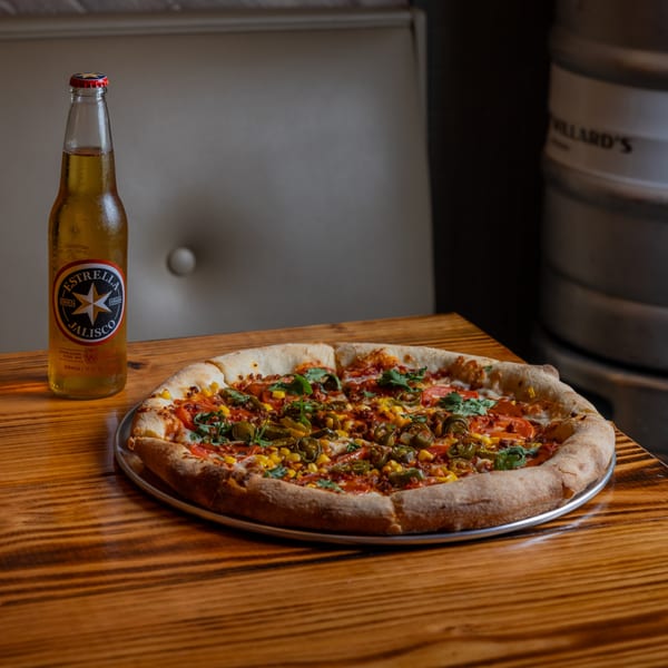A Heights Pizzeria pizza with jalapeños, corn, and cilantro, next to a bottle of Estrella Jalisco beer.
