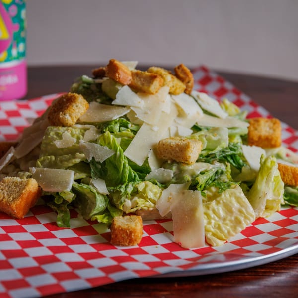 A Caesar salad with romaine lettuce, croutons, and parmesan cheese on a red and white checkered paper.