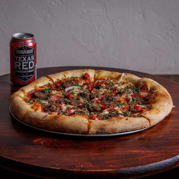 The Heights Pizzeria's pizza with meat, red peppers, and onions, next to a Texas Red beer can.
