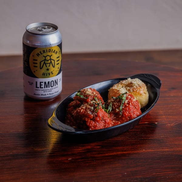 Meatballs in red sauce with basil and Parmesan, garlic knots, and a Meridian Hive Lemon wine cocktail.