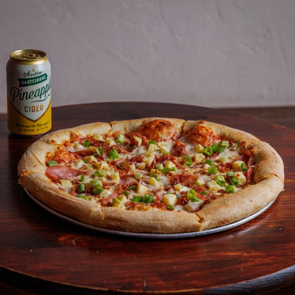 A pineapple, ham, and green onion pizza next to an Austin Eastciders Pineapple Cider can.