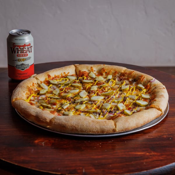 A Heights Pizzeria cheeseburger pizza with pickles and mustard, next to a can of Boulevard beer.