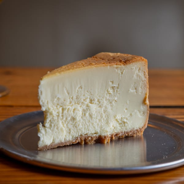 A slice of classic cheesecake with a graham cracker crust on a silver plate.
