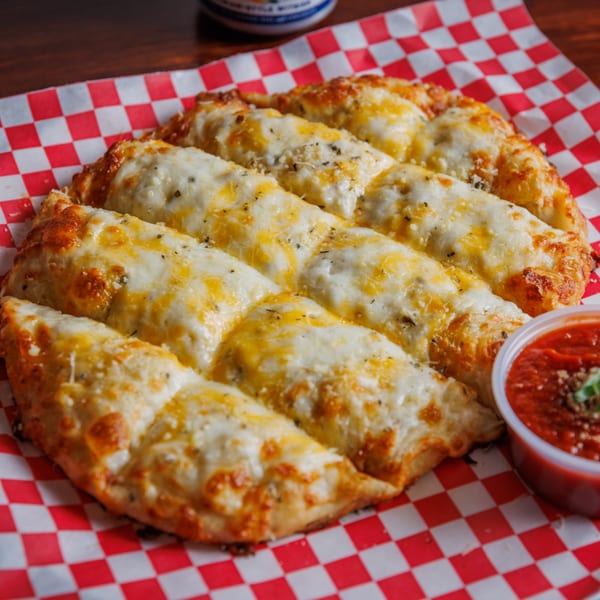 Cheesy garlic breadsticks with a side of marinara sauce on red and white checkered paper.